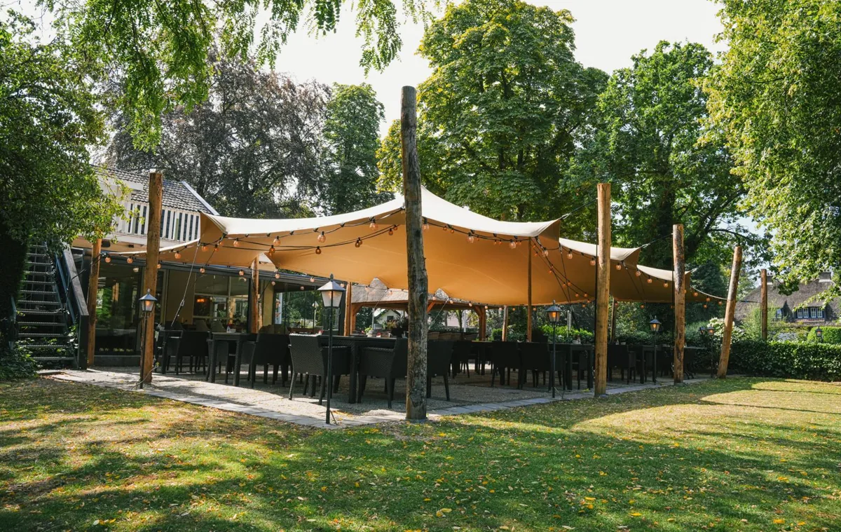 Stretch tent with festoon lights over a garden terrace, held up by timber poles