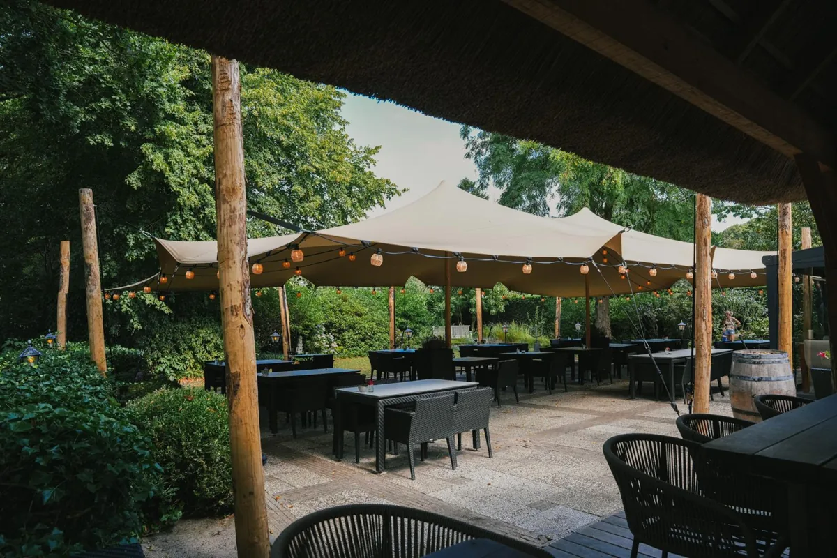 Cream stretch tent with lantern lights over a garden terrace, seen from under a thatched roof
